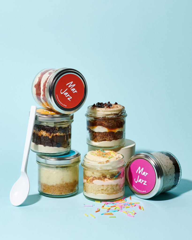 Small jars with dessert layers and colorful labels on a light blue background